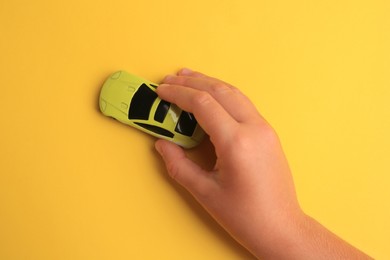 Child playing with toy car on yellow background, top view