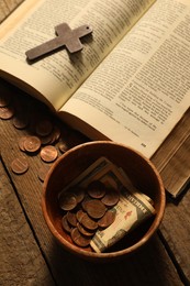 Photo of Donate and give concept. Bowl with coins, dollar banknotes, cross and Bible on wooden table, above view