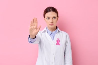 Photo of Mammologist with pink ribbon showing stop gesture against color background. Breast cancer awareness