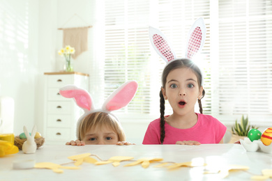 Emotional children wearing bunny ears headbands at table with Easter eggs, indoors