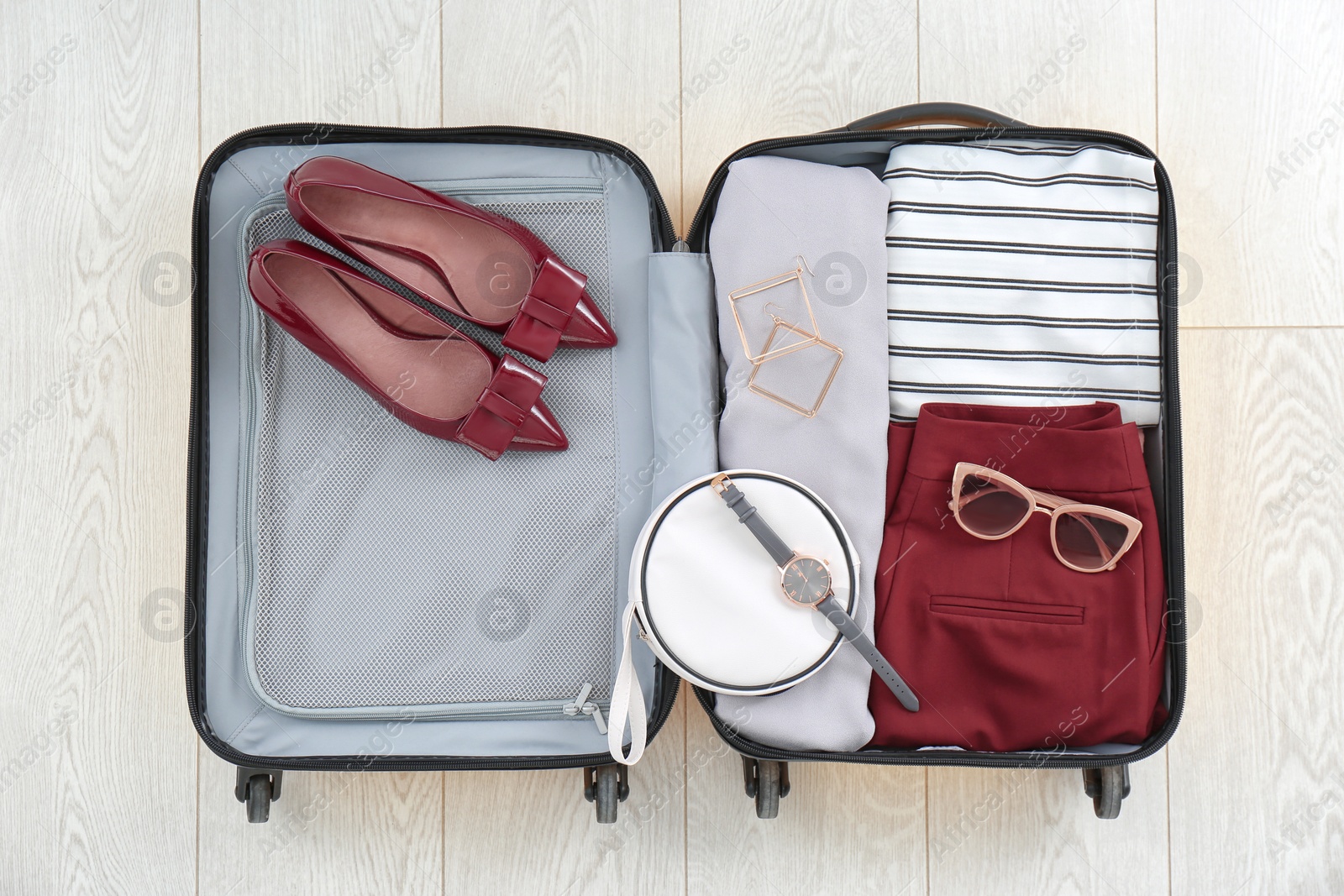 Photo of Open suitcase with female clothing, shoes and accessories on wooden background