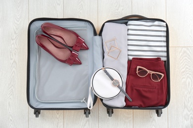 Open suitcase with female clothing, shoes and accessories on wooden background