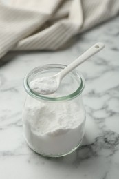 Baking powder in jar and spoon on white marble table, closeup