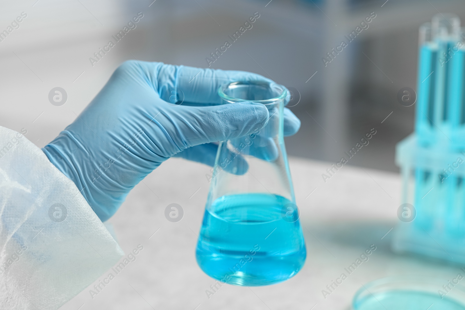 Photo of Scientist with beaker of light blue liquid in laboratory, closeup