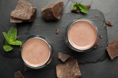 Glasses of delicious hot chocolate, chunks and fresh mint on black table, flat lay