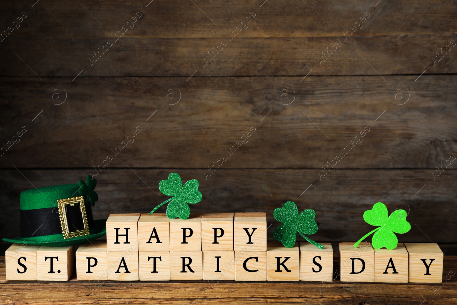 Photo of Wooden cubes with words HAPPY ST PATRICK'S DAY, green leprechaun hat and clover leaves on table