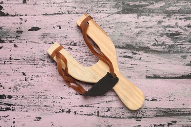 Slingshot with leather pouch on old pink wooden background, top view