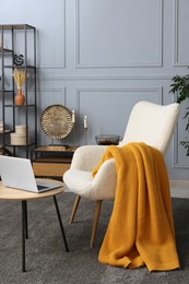 Photo of Living room interior with comfortable armchair, blanket and side table