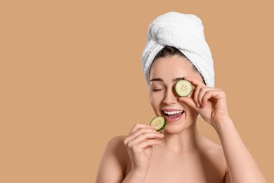Photo of Woman with towel holding pieces of cucumber on beige background, space for text. Spa treatment