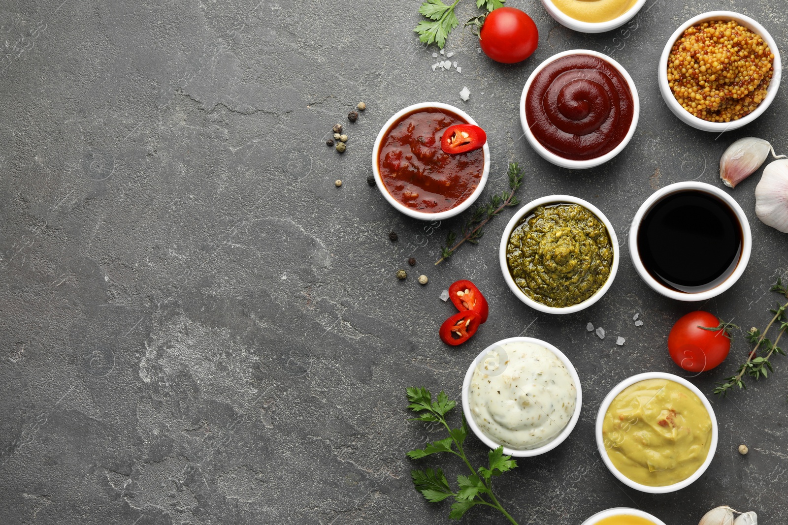 Photo of Many different sauces and spices on grey table, flat lay