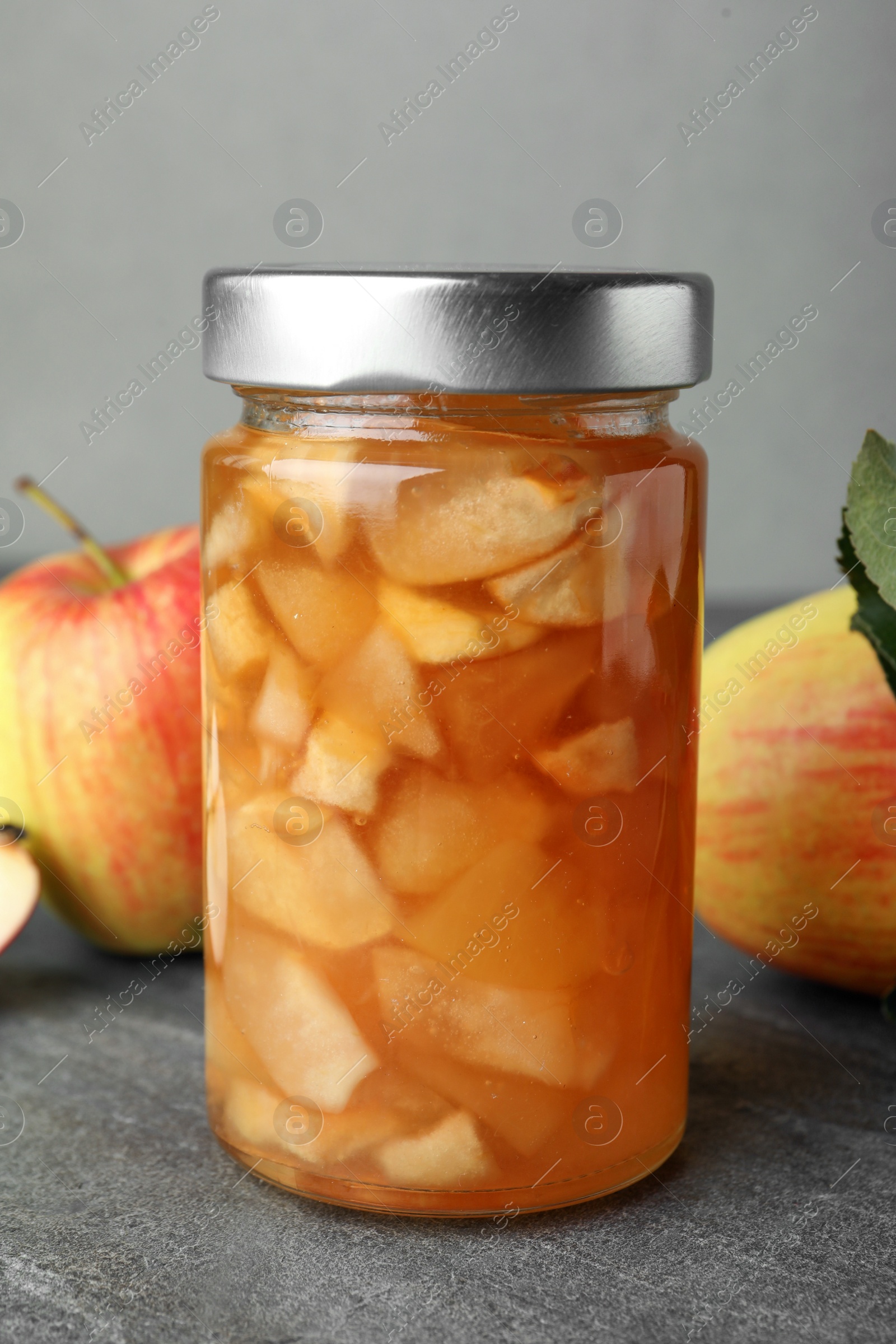 Photo of Tasty apple jam in glass jar on grey table