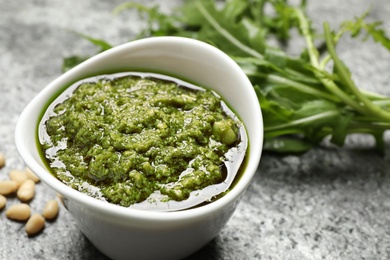 Photo of Bowl of tasty arugula pesto on grey table, closeup