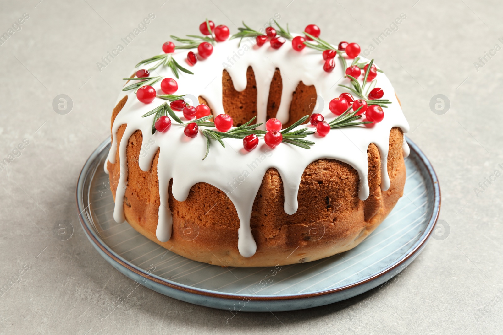 Photo of Traditional Christmas cake decorated with glaze, pomegranate seeds, cranberries and rosemary on light grey table