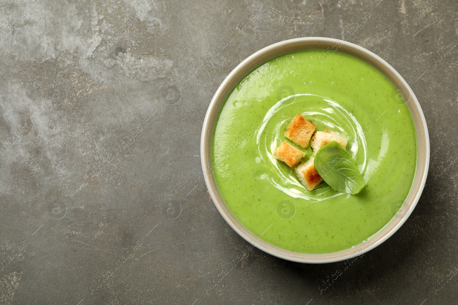 Photo of Tasty homemade zucchini cream soup on grey table, top view. Space for text