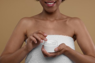 Photo of Young woman holding body cream on beige background, closeup