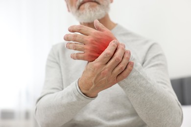 Senior man suffering from pain in wrist indoors, closeup