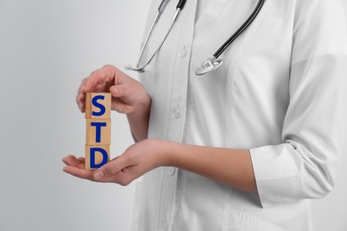 Photo of Doctor holding wooden cubes with abbreviation STD on white background, closeup