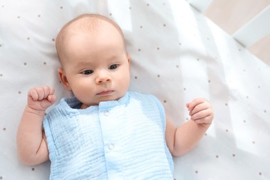 Photo of Cute little baby lying in crib at home, top view