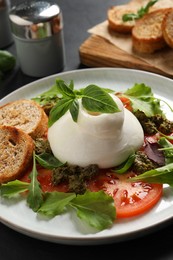 Photo of Delicious burrata salad with tomatoes, arugula and pesto sauce on dark grey table, closeup