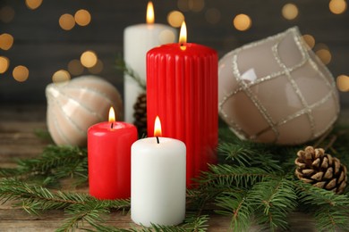 Photo of Burning candles and festive decor on wooden table against blurred Christmas lights