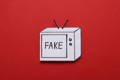 Paper TV with word Fake on red background, top view. Information warfare concept