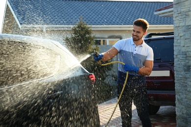 Young happy man washing car at backyard on sunny day