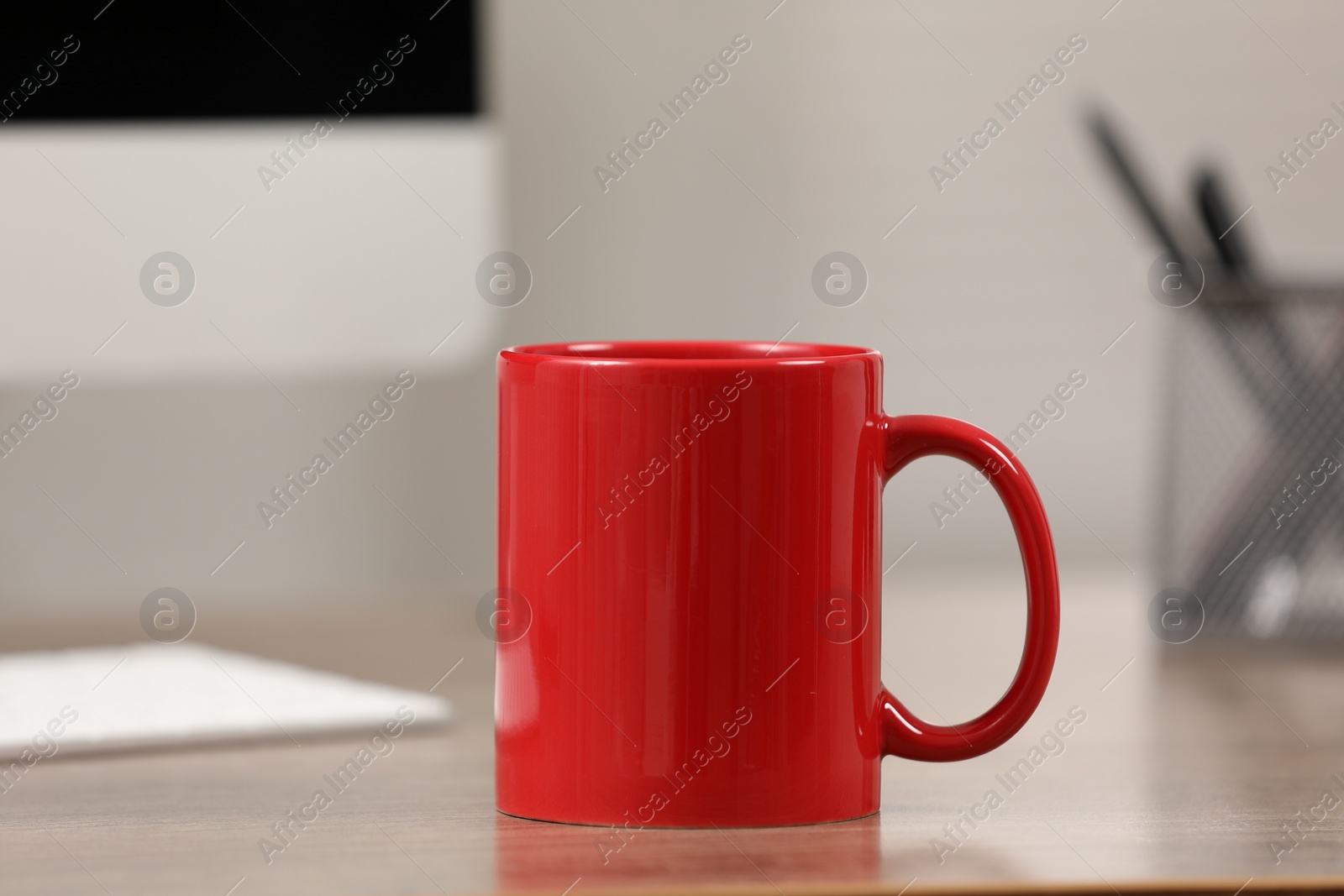 Photo of Red ceramic mug on wooden table at workplace