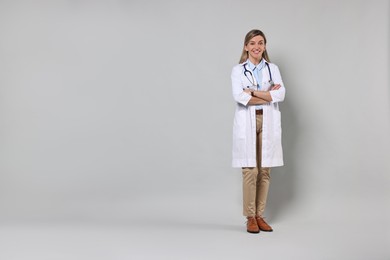 Portrait of happy doctor with stethoscope on light grey background, space for text