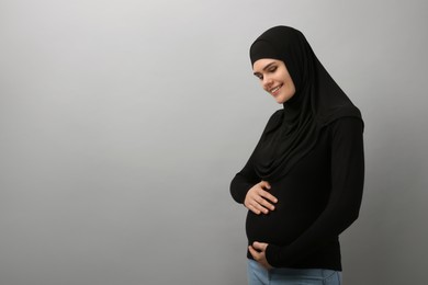 Photo of Portrait of pregnant Muslim woman in hijab on light gray background, space for text