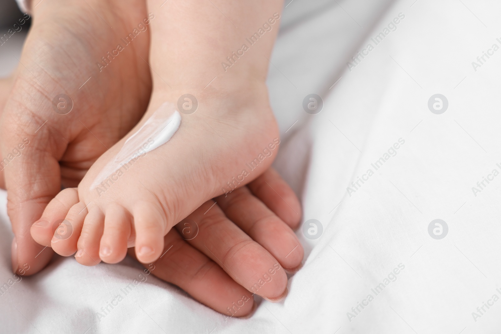 Photo of Woman applying body cream onto baby`s foot on bed, closeup