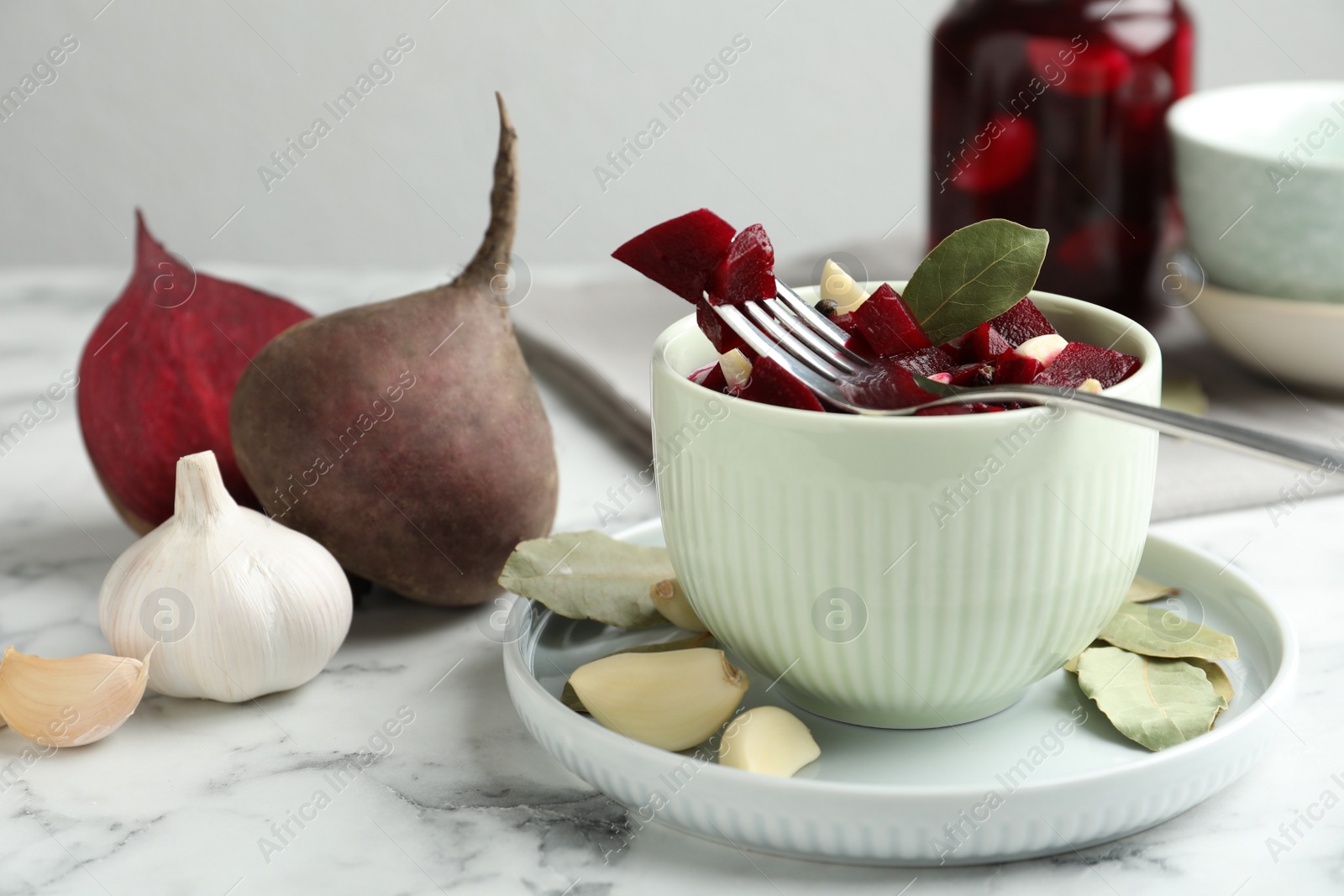 Photo of Pickled beets with garlic in bowl on white marble table