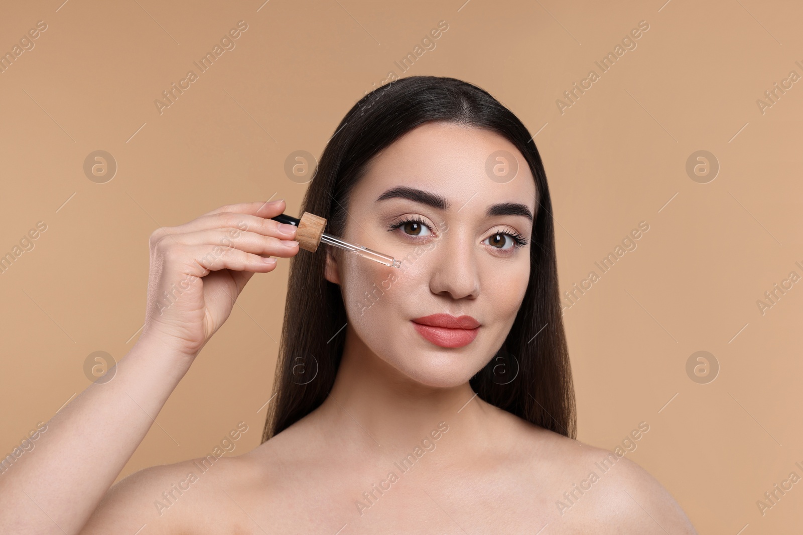 Photo of Young woman applying essential oil onto face on beige background