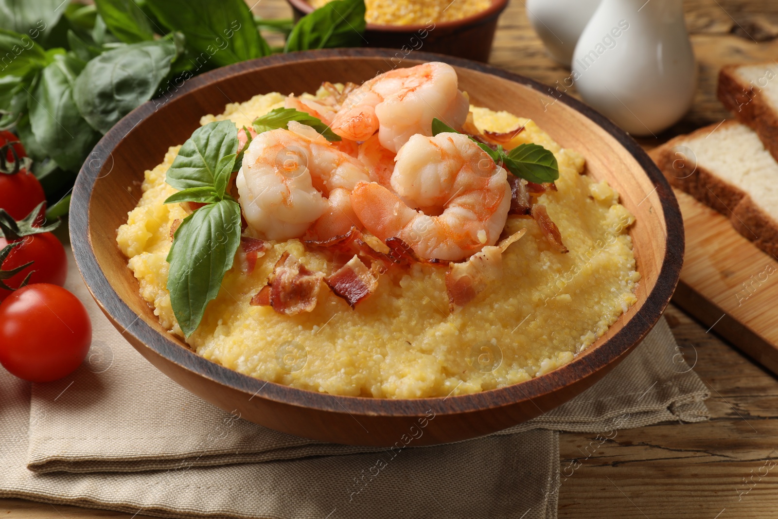 Photo of Fresh tasty shrimps, bacon, grits and basil in bowl on wooden table, closeup