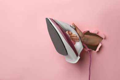 Photo of Woman holding modern iron through hole in pink paper, closeup. Space for text