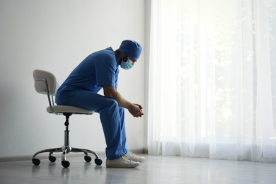 Photo of Exhausted doctor sitting on chair indoors, space for text. Stress of health care workers during COVID-19 pandemic
