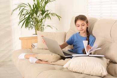 Girl with laptop and book on sofa at home