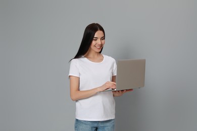 Young woman with modern laptop on light grey background