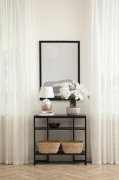 Photo of Blooming orchid and lamp on console table indoors. Interior design