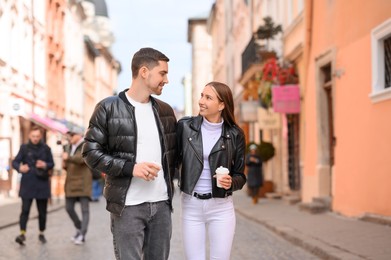 Photo of Lovely young couple with cups of coffee walking together on city street. Romantic date