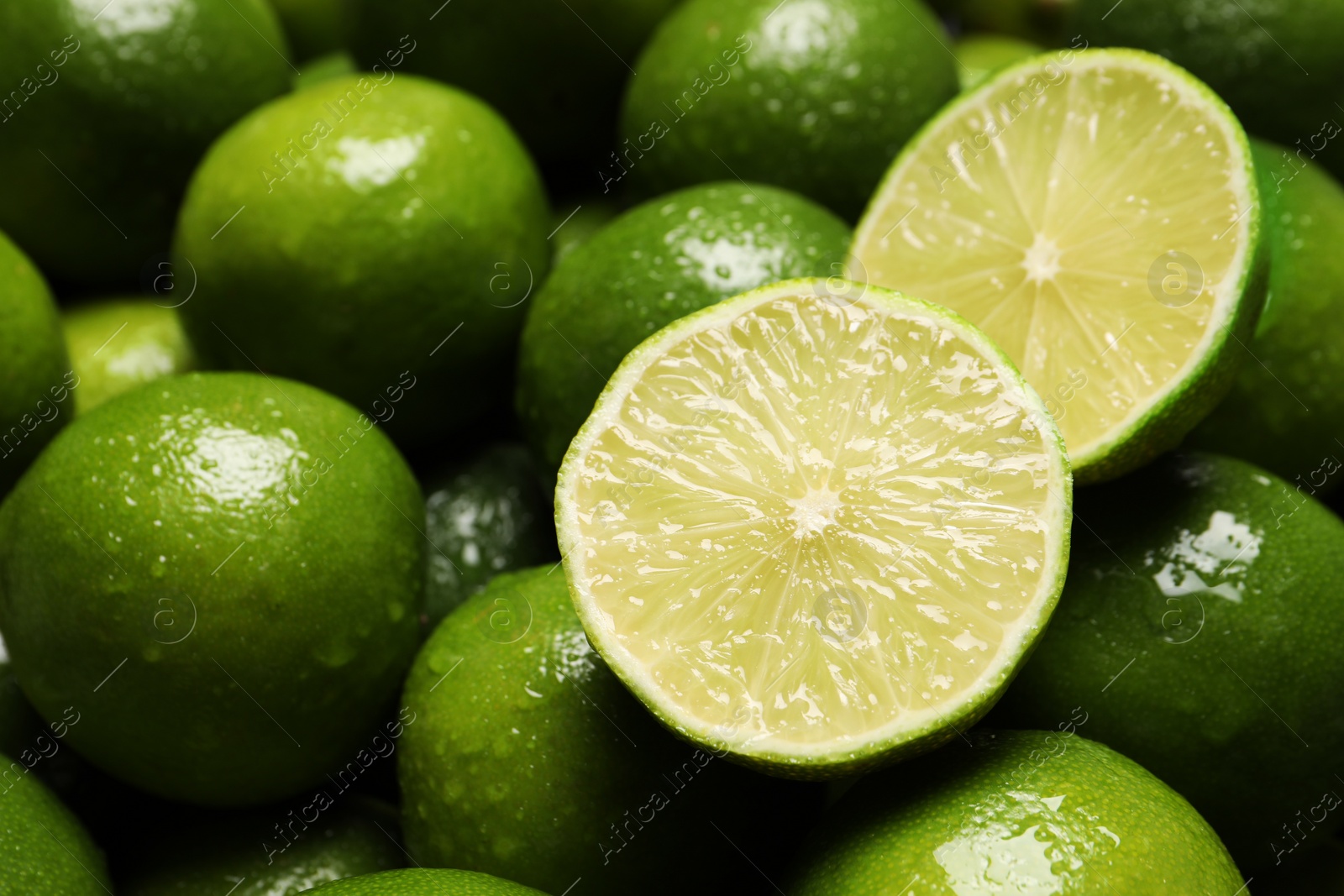 Photo of Whole and cut fresh limes with water drops as background, closeup