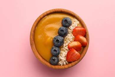Photo of Delicious smoothie bowl with fresh berries and coconut flakes on pale pink background, top view