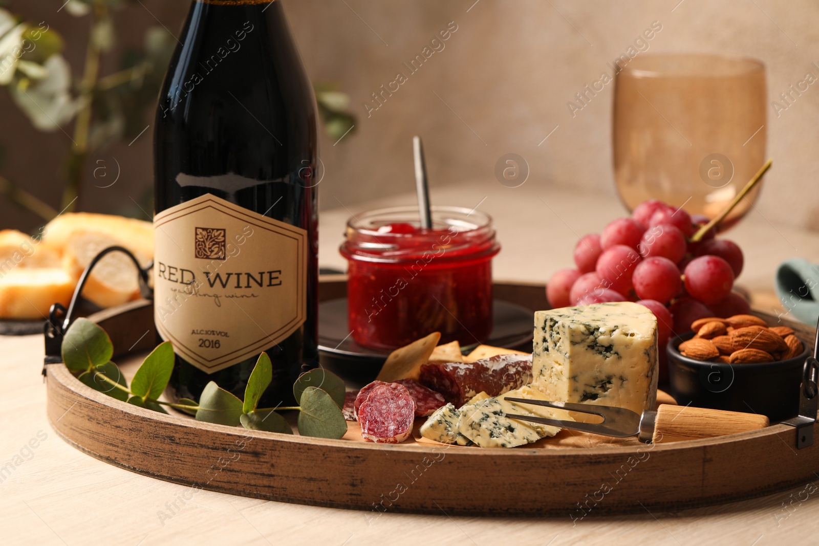 Photo of Bottle of red wine and delicious snacks on wooden table, closeup