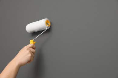 Photo of Worker using roller to paint wall with grey dye, closeup. Space for text