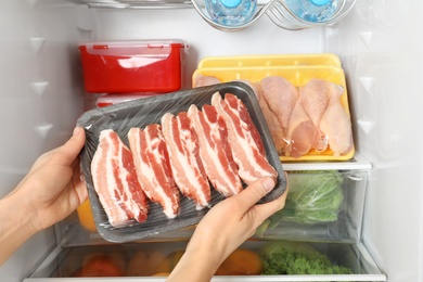 Photo of Woman taking raw bacon from refrigerator, closeup