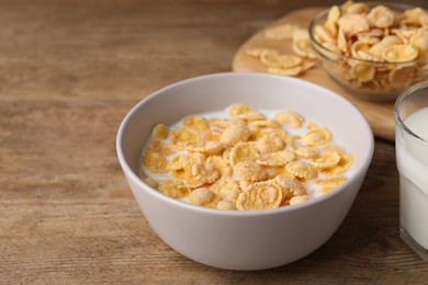 Photo of Tasty cornflakes with milk in bowl on wooden table, space for text