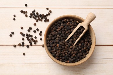 Aromatic spice. Black peppercorns and scoop in bowl on wooden table, top view