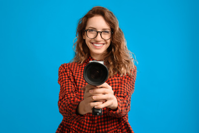 Beautiful young woman with vintage video camera against light blue background, focus on lens