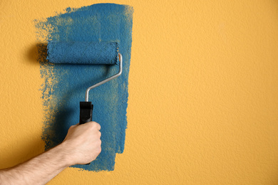 Photo of Man painting yellow wall with blue dye, closeup. Space for text