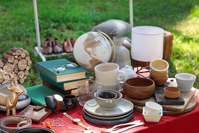 Photo of Many different items on red tablecloth outdoors. Garage sale