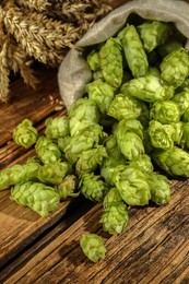 Photo of Overturned sack of hop flowers and wheat ears on wooden table, closeup